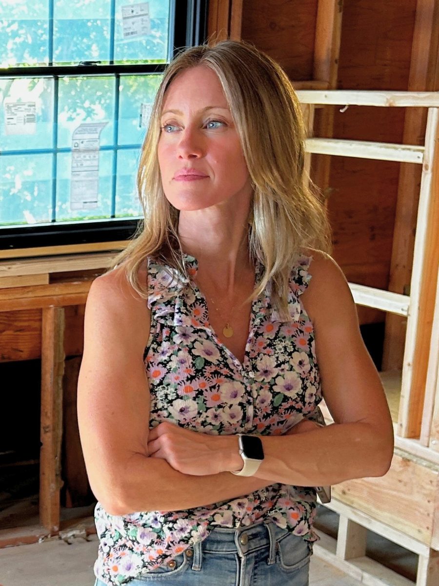 Jess standing with her arms crossed by a window in a house stripped to the studs.