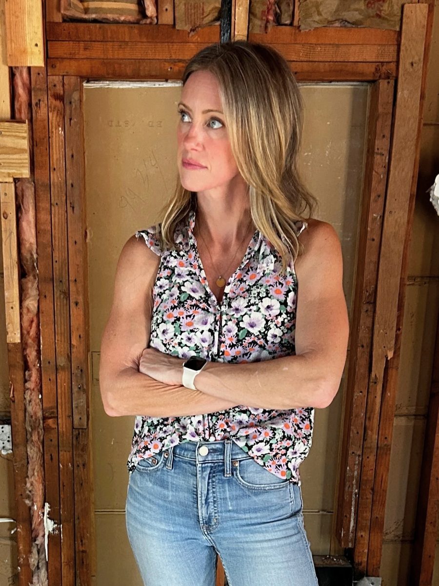 Jess standing with her arms crossed in a house stripped to the studs, surveying the space.